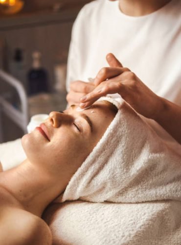 Beautician applying facial cream all over young woman's forehead at spa salon. Skin treatment. Girl facial treatment. Medical health.